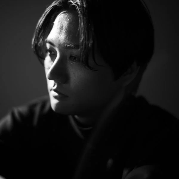 強い光と影が特徴的なモノクロポートレート。若い男性の横顔が捉えられ、思慮深く、どこか憂いを帯びた表情が印象的です。