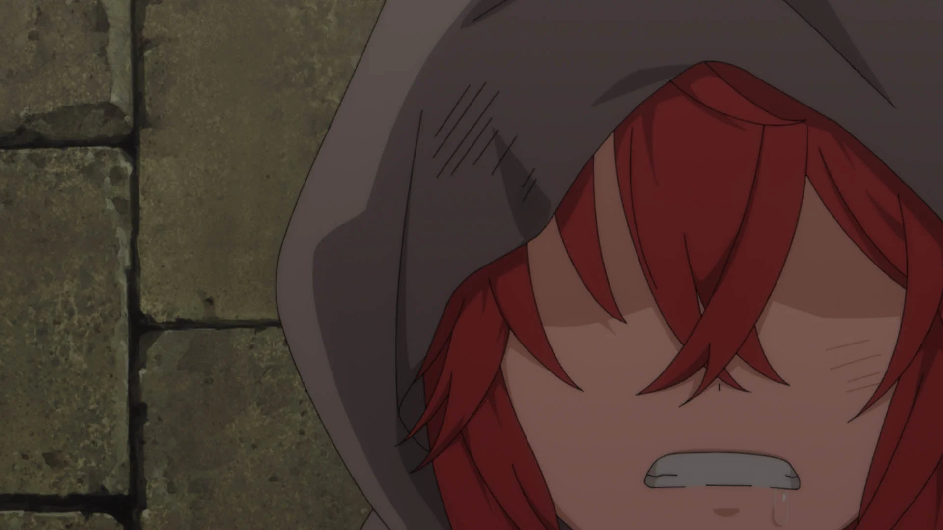 赤い髪のキャラクターがフードをかぶり、悲しげな表情で泣いているアニメの一場面です。顔は髪とフードで一部隠れており、背景は石造りの壁のようです。