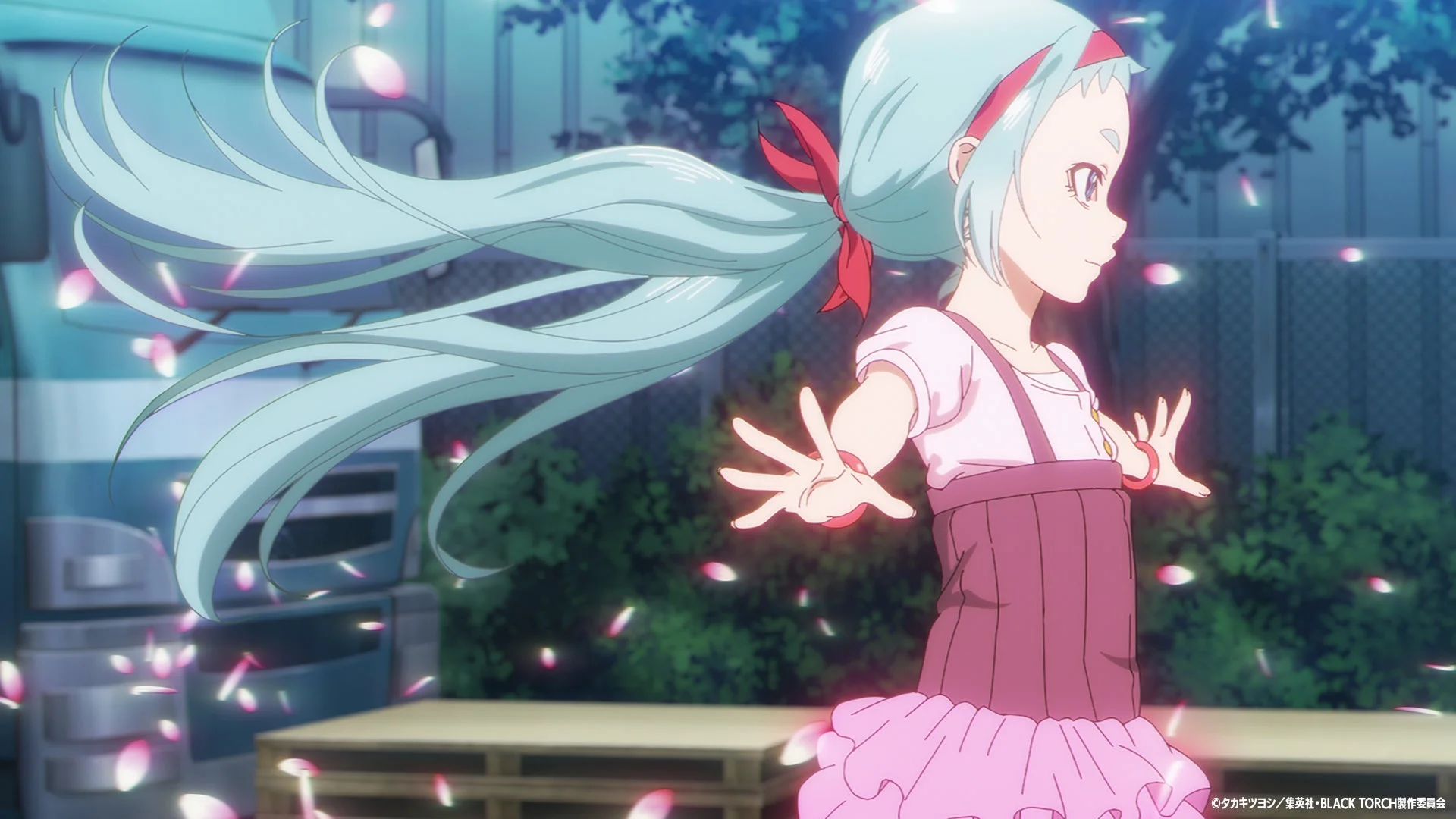 水色のロングヘアの少女が、舞い散るピンクの花びらの中で、軽やかに両手を広げているアニメーションの一場面。背景にはトラックと暗い木々が見え、幻想的な雰囲気です。