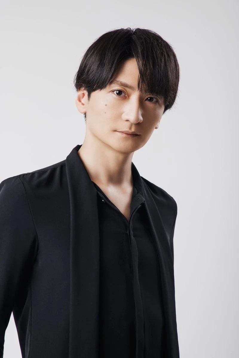 黒いシャツを着用し、カメラをまっすぐ見つめる黒髪の男性のポートレートです。背景はシンプルな白で、落ち着いた表情が印象的です。